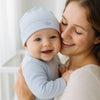 Mama hält lachendes Baby mit blauer Baby Corner Mütze (Krone-Stickerei) im Arm – kuschelige Baumwolle, One Size; warm, bequem und ideal für die Erstausstattung.