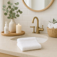 Weißer ebelin Frottee-Waschhandschuh im Badezimmer auf dem Waschbeckenrand – sanfte Babypflege, praktisch für die Erstausstattung und ein liebevolles Geburtsgeschenk.