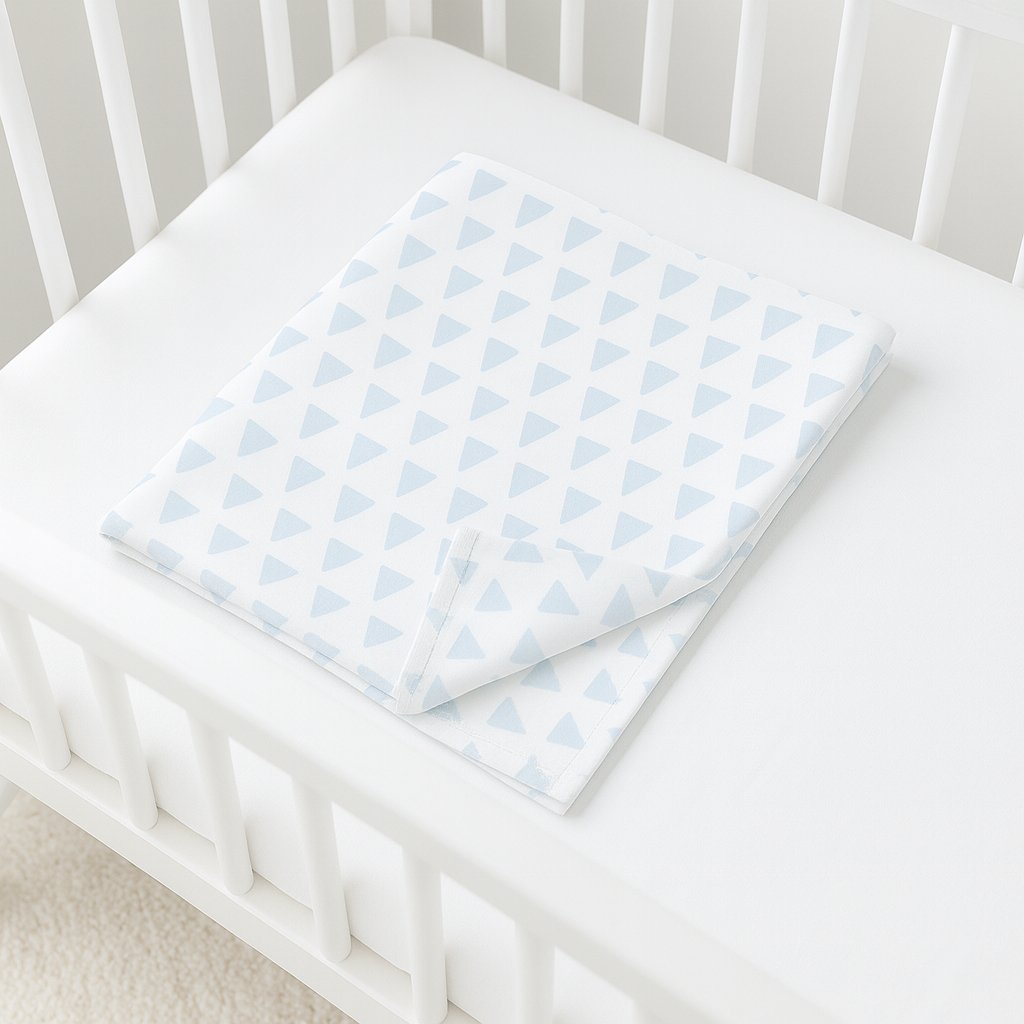 Julius Zöllner Jersey-Babydecke mit hellblauem Dreieckmuster gefaltet im weißen Gitterbett – 100 % Baumwolle, Oeko-Tex Klasse 1, ideal für Kinderwagen/Wiege.