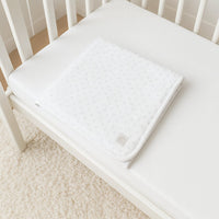 Weiße Julius Zöllner Jersey-Babydecke mit grauen Herzchen gefaltet im Babybett; 100 % Baumwolle, Oeko-Tex Klasse 1 – weiche Zudecke für unterwegs und Zuhause.