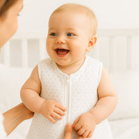 Lachendes Baby im Julius Zöllner Schlafsack, weiß mit Punkt-Print, Größe 70 cm; Elternteil schließt den Reißverschluss – gemütliche Erstausstattung fürs Babybett.