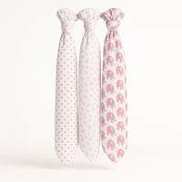 Drei Musselin Swaddle-Tücher von Julius Zöllner, 120×120 cm, weiß/rosa mit Herz-, Dreieck- und Elefanten-Print, nebeneinander aufgehängt – ideal für Erstausstattung/Geschenk zur Geburt.