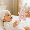 Baby greift nach dem rosa Maximo Greifring Hase – weiches Greifspielzeug, schönes Geschenk zur Geburt.