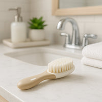 Beige NUK Babybürste mit weichen Nylonborsten liegt im Bad-Ambiente – sanfte Pflege für Babys, praktisches Pflegetool für frischgebackene Eltern, tolles Geburtsgeschenk und Ergänzung für die Baby Box.