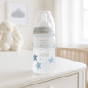 NUK Babyflasche 300 ml mit beigem Ring und Sternen liegt auf der Kommode im hellen Babyzimmer – hygienisch, leicht und praktisch, ideale Ergänzung für die Babyerstausstattung und die Baby Box.