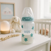 NUK Babyflasche 300 ml mit grünem Ring und Sternen steht im Kinderzimmer auf der Kommode; mit Milch befüllt – praktischer Begleiter für Neugeborene und Babys, tolle Ergänzung für die Baby Box und Elternalltag.
