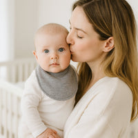 Baby auf dem Arm trägt graues Pippi Babyhalstuch (One Size) mit Druckknopf – kuscheliges Lätzchen gegen Sabbern, passende Ergänzung zur Erstausstattung, schönes kleines Geschenk zur Geburt.