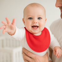 Baby auf dem Arm trägt rotes Pippi Babyhalstuch – weiches, saugfähiges Lätzchen mit Druckknopf, ideal fürs Zahnen, Baby Box und als Geschenk zur Geburt.