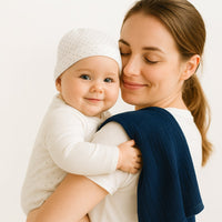 Mama hält Baby im Arm, über der Schulter liegt die dunkelblaue Pippi Mullwindel (70×70 cm) – sanftes Spucktuch aus Baumwolle, perfekt als Geburtsgeschenk.