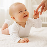 Baby trägt weiße Erstlingssöckchen von Playshoes, 0–3 Monate, in hellem Schlafzimmer – passende Erstausstattung für Neugeborene.