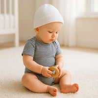 Baby sitzt auf hellem Teppich und trägt einen blau-weiß geringelten Sanetta Kurzarm-Body aus GOTS-zertifizierter Bio-Baumwolle; weiche Feinrippqualität mit praktischem Amerikanerausschnitt – ideal für den Alltag und sensible Haut.