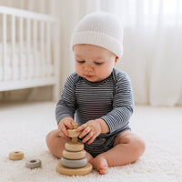 Baby in blau-weiß gestreiftem Sanetta Langarm-Body sitzt im Kinderzimmer auf dem Teppich und spielt mit Holz-Steckringen – Bio-Baumwolle GOTS, angenehme Feinripp-Qualität, praktischer US-Ausschnitt und Druckknöpfe im Schritt, pflegeleicht und trocknerfest.