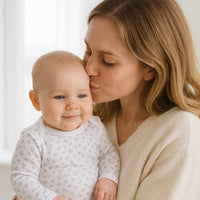 Mama küsst ihr Baby im weißen Sanetta Langarmbody mit feinem Blumenprint – weiche Bio-Baumwolle, ohne Seitennähte und mit nickelfreien Druckknöpfen; ideal für empfindliche Babyhaut und die erste Ausstattung.