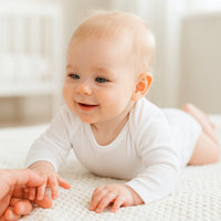 Weißer Schnizler Langarm-Body am Baby in Bauchlage auf weicher Decke – sanfte Interlock-Qualität, hautfreundlich und bequem; perfektes Alltags-Basic für die Erstausstattung.