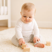 Baby in beiger, gestreifter Schnizler Hose Größe 62 sitzt auf weichem Teppich und spielt mit Holzbausteinen – weicher Umschlagbund, elastische Bündchen, angenehm auf der Haut und pflegeleicht.