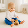 Baby trägt blaue Schnizler Babyhose und spielt auf hellem Teppich mit Holz-Ringturm im Babyzimmer – bequeme Baumwollhose Größe 62 für Alltag und Krabbelzeit.