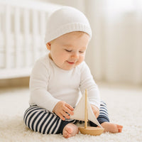 Baby trägt navy-weiß gestreifte Schnizler Babyhose und spielt auf hellem Teppich mit Holz-Segelboot im Babyzimmer – bequeme Baumwollhose Größe 62 für Alltag und Krabbelzeit.