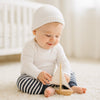 Baby trägt navy-weiß gestreifte Schnizler Babyhose und spielt auf hellem Teppich mit Holz-Segelboot im Babyzimmer – bequeme Baumwollhose Größe 62 für Alltag und Krabbelzeit.
