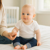 Baby sitzt mit navyfarbener Sense Organics Hose (62–68 cm) auf dem Bett, gestreifter Umschlagbund – weiche Bio-Baumwolle, ideal für Geburtsgeschenk oder Baby Box.